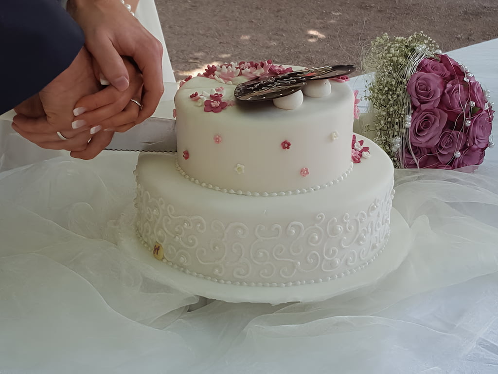 Ein Hochzeitspaar schneidet mit aufeinanderliegenden Händen seine Torte an.