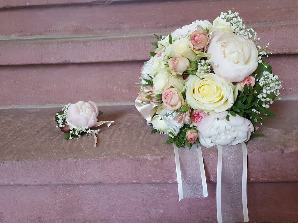 Auf einer steinernen Treppe liegen Ansteckblume des Bräutigams und Brautstrauss